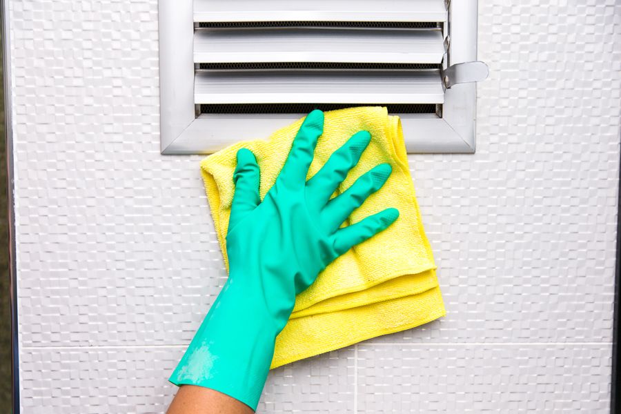 Image of someone cleaning an air duct with green gloves and a yellow cloth. Air Duct Cleaning.